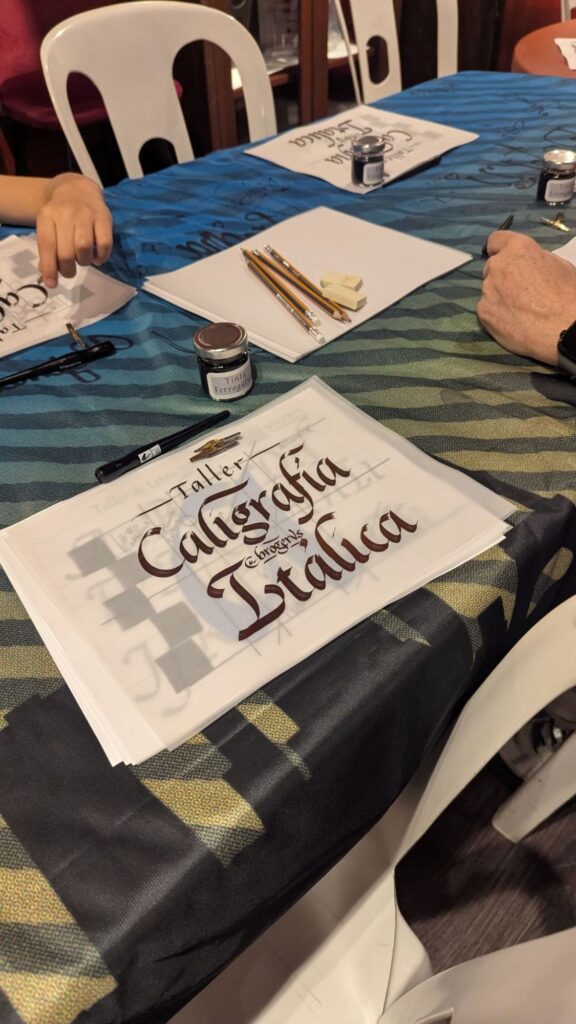 Mesa de un taller presencial de caligrafía itálica con plumillas, tinta y hojas de práctica